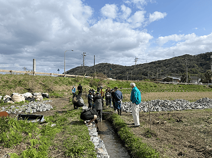 画像：石積みの排水路で小学生が生き物観察をしている様子