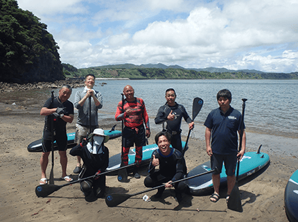  画像：浜辺でSUPを背にして記念撮影する様子