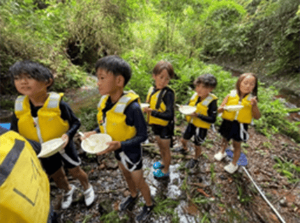 画像：通潤橋の源流において、子供たちがカグヤ米の白ごはんをメインに発芽玄米の冷や味噌汁と、ふりかけでランチをしている様子